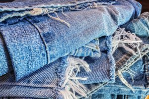 An abstract pile of several different pairs of old, used, ragged, worn and torn blue jeans ready to be recycled.