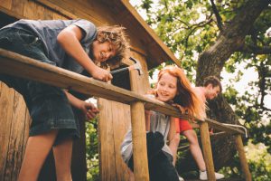 Friends who are children working together to build a treehouse, hammering, helping and sawing on a summer day
